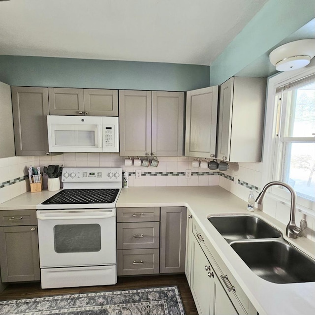 kitchen with white appliances, decorative backsplash, a sink, and gray cabinetry