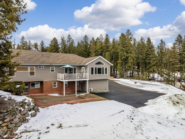 snow covered rear of property featuring driveway, a deck, and brick siding