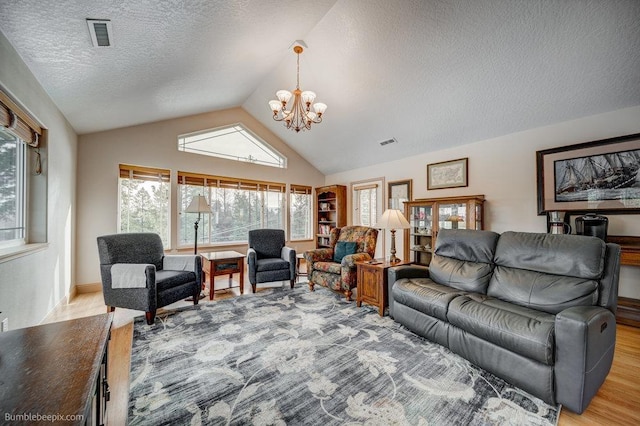 living area with a textured ceiling, light wood-style flooring, lofted ceiling, a notable chandelier, and visible vents