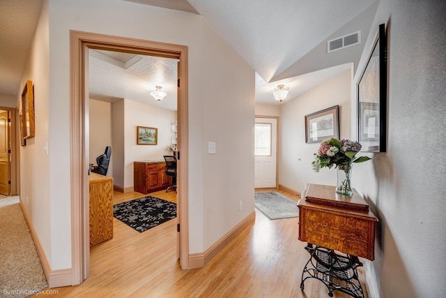 foyer featuring visible vents, light wood-style flooring, vaulted ceiling, a textured ceiling, and baseboards