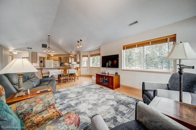 living area featuring vaulted ceiling, a textured ceiling, light wood-type flooring, and visible vents