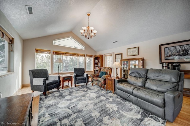 living area featuring a notable chandelier, lofted ceiling, visible vents, light wood-style flooring, and a textured ceiling