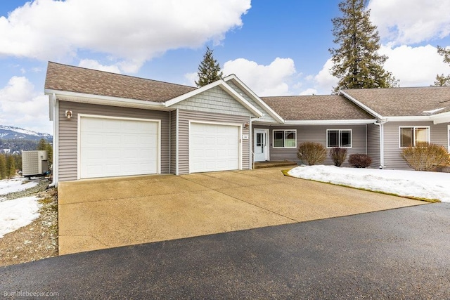 ranch-style home with an attached garage, a shingled roof, central AC, and concrete driveway