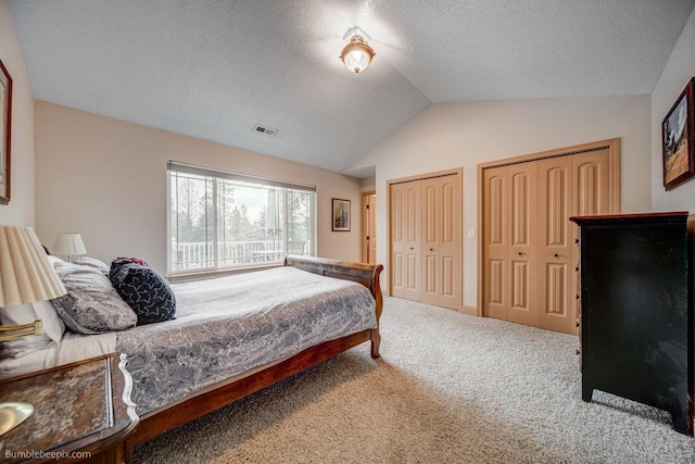 bedroom with carpet, two closets, lofted ceiling, visible vents, and a textured ceiling