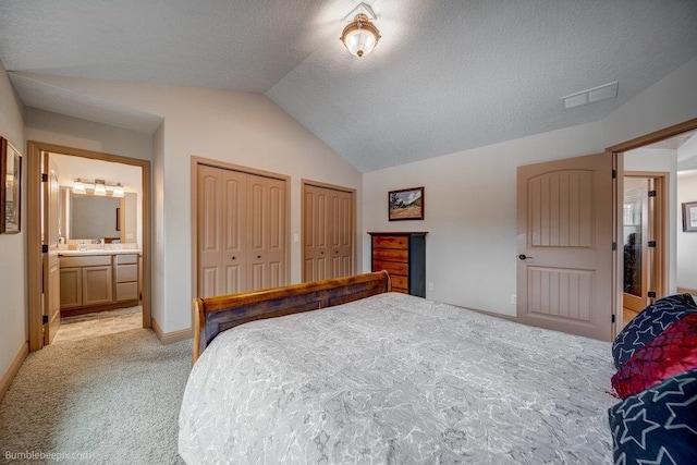 bedroom with visible vents, connected bathroom, light colored carpet, lofted ceiling, and multiple closets