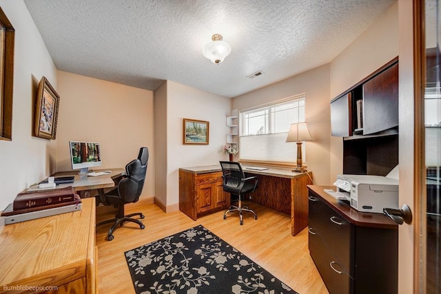 office area featuring baseboards, light wood-style flooring, visible vents, and a textured ceiling