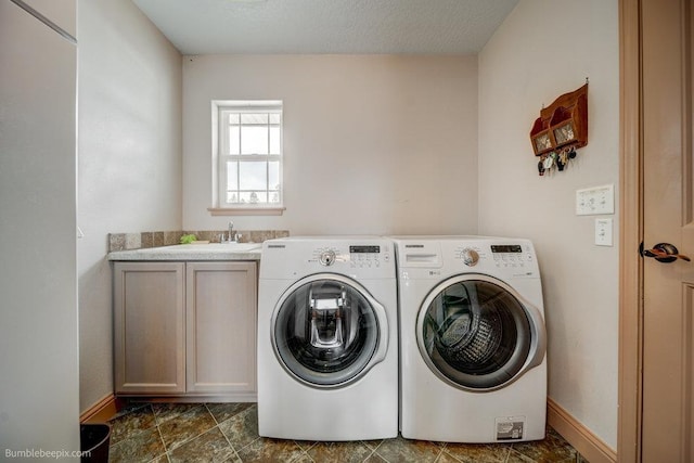 washroom featuring cabinet space, baseboards, washing machine and clothes dryer, a textured ceiling, and a sink