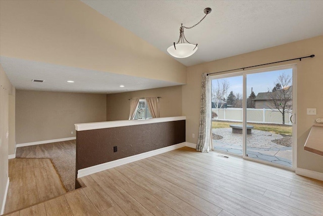 spare room featuring vaulted ceiling, light wood finished floors, visible vents, and baseboards