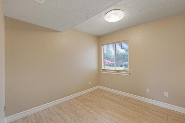 spare room featuring light wood-style flooring, baseboards, and a textured ceiling