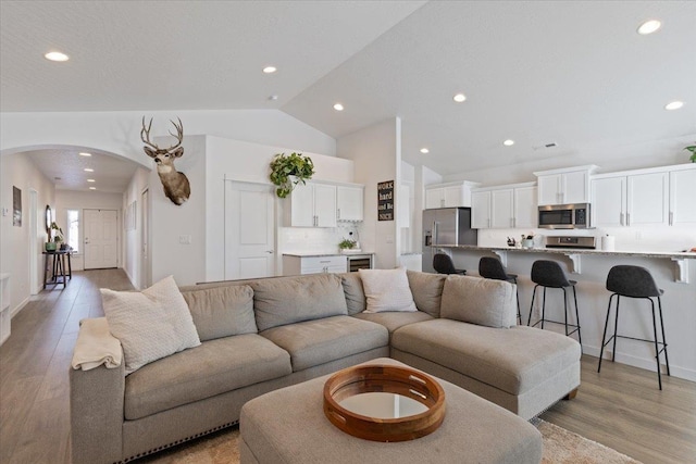 living room featuring arched walkways, vaulted ceiling, light wood finished floors, and recessed lighting