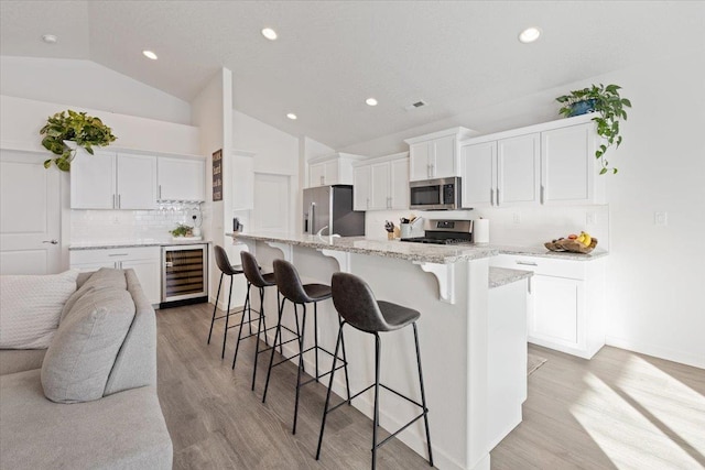 kitchen featuring beverage cooler, appliances with stainless steel finishes, a center island with sink, and white cabinetry