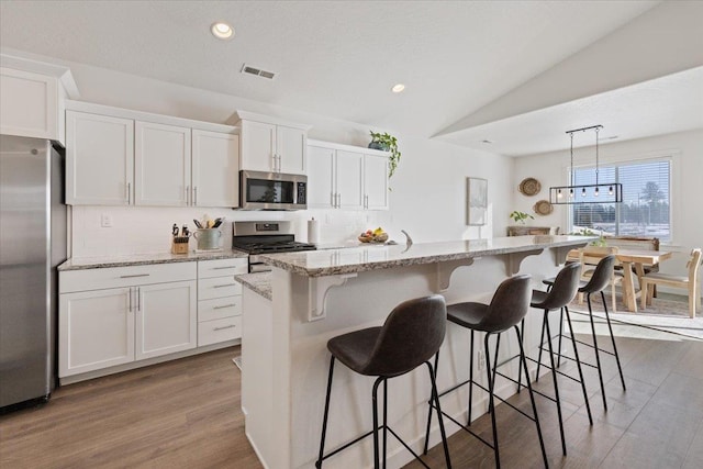 kitchen with lofted ceiling, a kitchen island with sink, stainless steel appliances, white cabinets, and pendant lighting