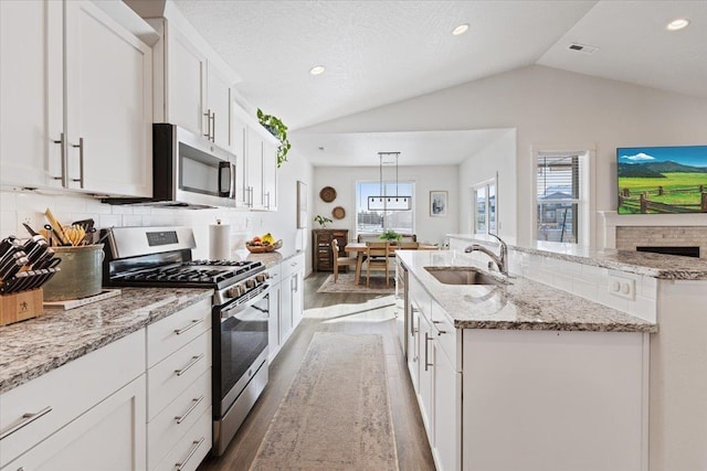 kitchen featuring stainless steel appliances, a sink, white cabinetry, hanging light fixtures, and an island with sink