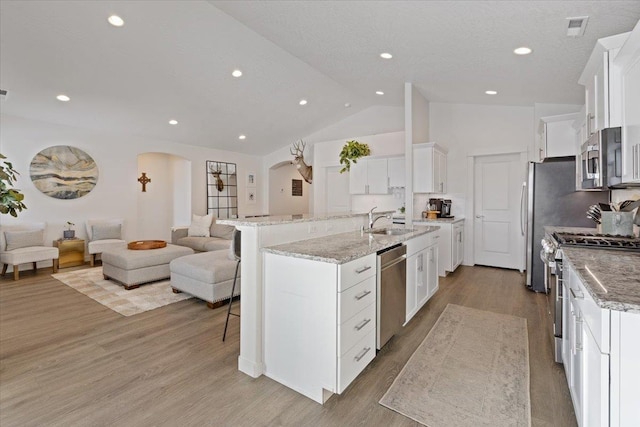 kitchen featuring arched walkways, a center island with sink, appliances with stainless steel finishes, open floor plan, and white cabinets