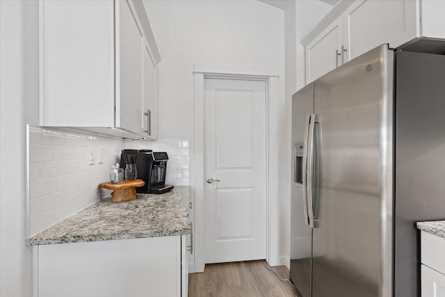 kitchen featuring tasteful backsplash, light wood-style flooring, white cabinets, light stone countertops, and stainless steel fridge with ice dispenser