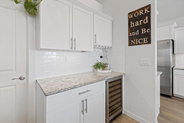 kitchen with wine cooler, light stone counters, freestanding refrigerator, light wood-type flooring, and white cabinetry