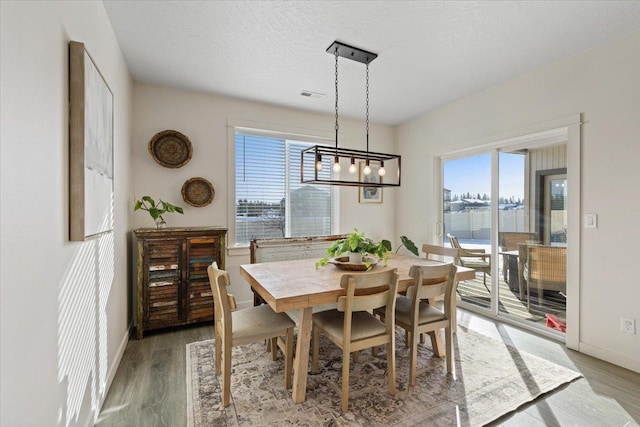 dining room featuring baseboards, a textured ceiling, visible vents, and wood finished floors