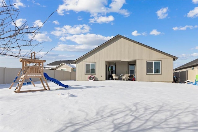 snow covered rear of property featuring a playground and fence