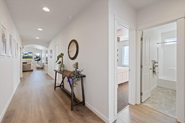 corridor featuring arched walkways, light wood-style flooring, baseboards, and recessed lighting