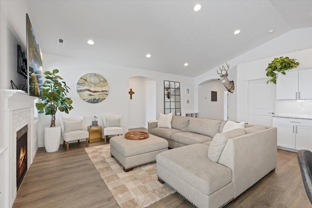 living area featuring arched walkways, lofted ceiling, visible vents, light wood-style flooring, and a brick fireplace