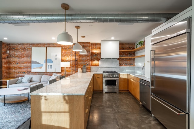 kitchen featuring premium appliances, light stone counters, decorative light fixtures, a peninsula, and wall chimney exhaust hood