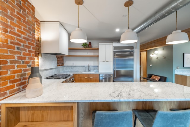 kitchen featuring a sink, appliances with stainless steel finishes, custom exhaust hood, light stone countertops, and decorative light fixtures