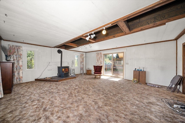 unfurnished living room with carpet floors, rail lighting, a wood stove, and a healthy amount of sunlight