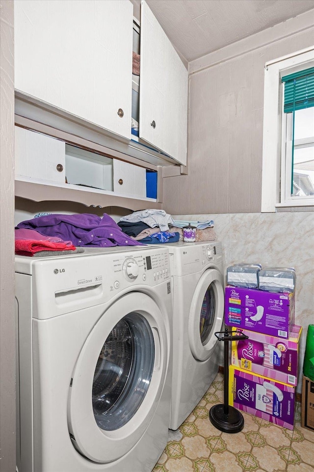 clothes washing area with light floors, washer and clothes dryer, and cabinet space