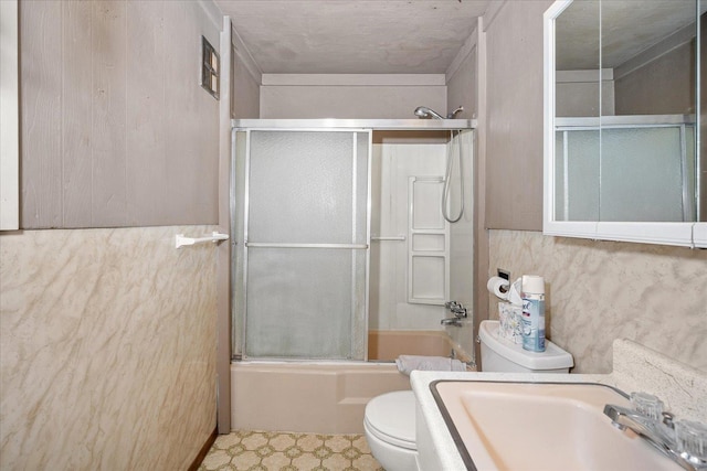 bathroom with toilet, bath / shower combo with glass door, a sink, and tile patterned floors