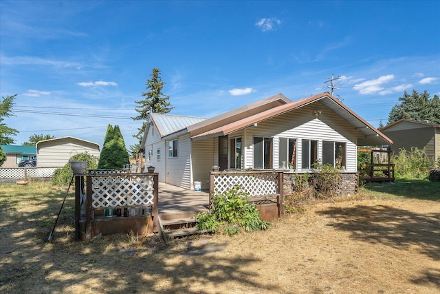 back of house with a deck, fence, and metal roof