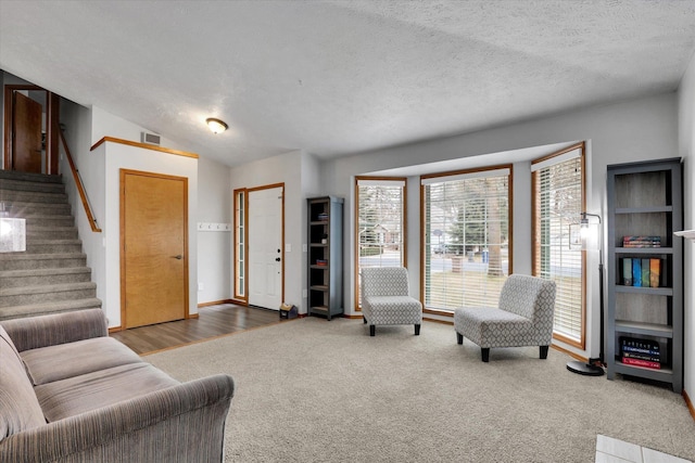 carpeted living area with visible vents, baseboards, stairway, vaulted ceiling, and a textured ceiling