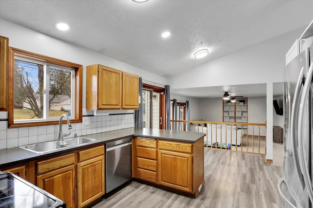 kitchen with a peninsula, a sink, vaulted ceiling, appliances with stainless steel finishes, and dark countertops