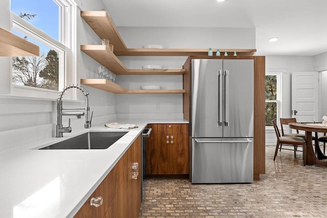 kitchen featuring open shelves, high end fridge, light countertops, brown cabinetry, and a sink