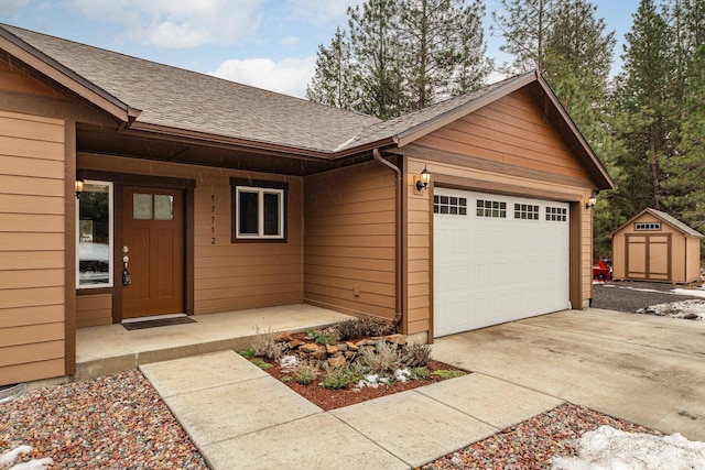 view of front of home with a garage, a storage shed, a shingled roof, driveway, and an outbuilding