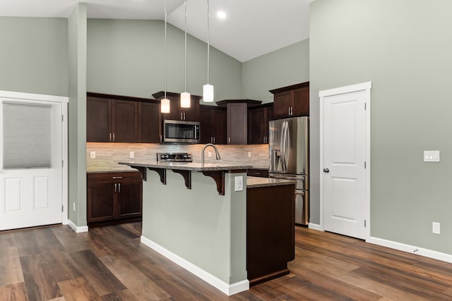 kitchen with high vaulted ceiling, stainless steel appliances, a kitchen breakfast bar, dark brown cabinets, and light stone countertops