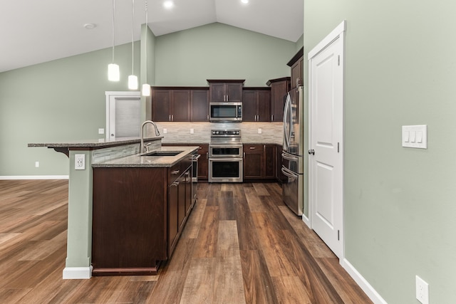 kitchen featuring dark brown cabinetry, a sink, appliances with stainless steel finishes, decorative backsplash, and dark stone countertops