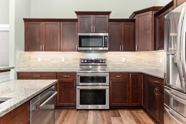 kitchen with dark wood-style floors, appliances with stainless steel finishes, light stone counters, dark brown cabinets, and backsplash