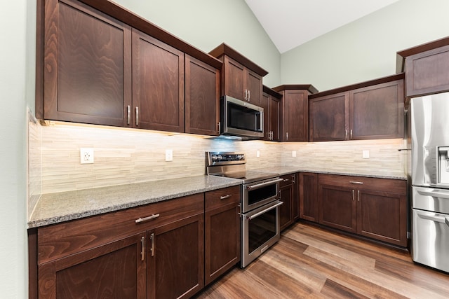 kitchen with lofted ceiling, light stone countertops, tasteful backsplash, and appliances with stainless steel finishes