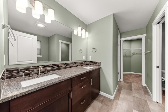 full bath with double vanity, backsplash, a sink, and baseboards