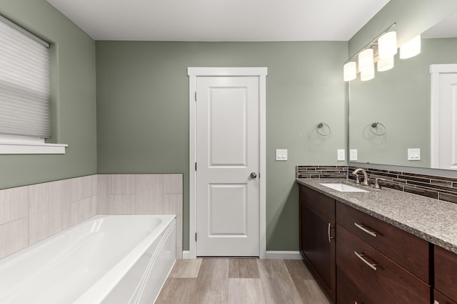 bathroom featuring tasteful backsplash, baseboards, wood finished floors, a garden tub, and vanity