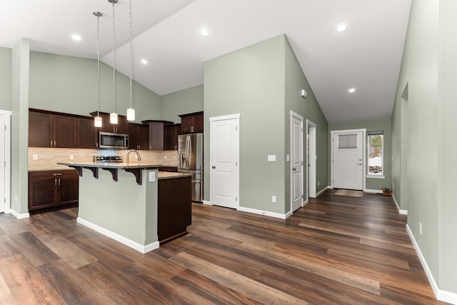 kitchen featuring high vaulted ceiling, dark wood-type flooring, a kitchen breakfast bar, dark brown cabinets, and appliances with stainless steel finishes