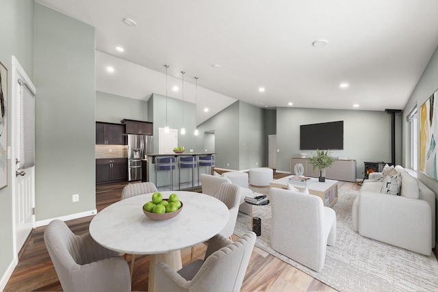 dining space featuring recessed lighting, a wood stove, wood finished floors, high vaulted ceiling, and baseboards