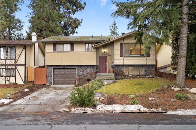 bi-level home with an attached garage, stone siding, a front lawn, and concrete driveway