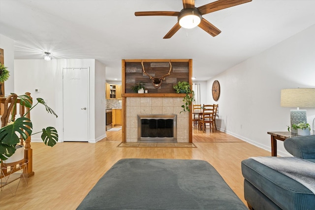 living area featuring baseboards, ceiling fan, a tile fireplace, and light wood-style floors