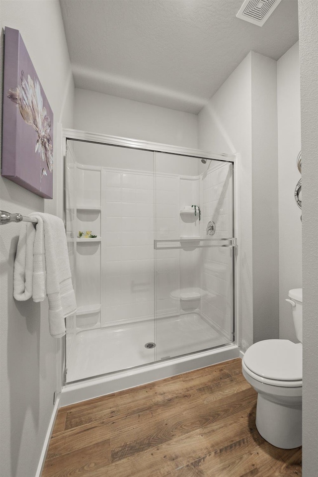 bathroom featuring visible vents, toilet, a textured ceiling, a shower stall, and wood finished floors