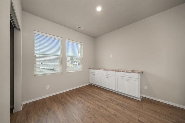 empty room with visible vents, a textured ceiling, baseboards, and wood finished floors