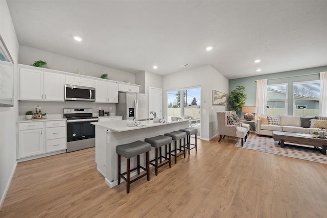 kitchen featuring a kitchen island with sink, white cabinetry, a kitchen breakfast bar, light countertops, and appliances with stainless steel finishes