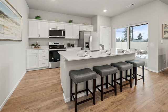 kitchen featuring white cabinets, a center island with sink, stainless steel appliances, and light countertops