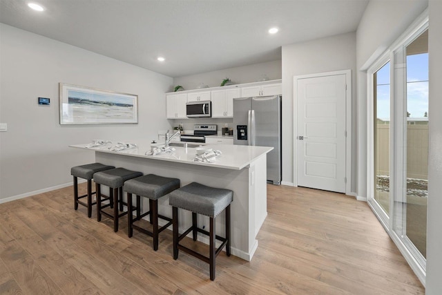 kitchen featuring a breakfast bar, a center island with sink, light countertops, appliances with stainless steel finishes, and white cabinets