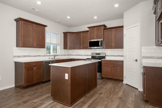 kitchen with a center island, dark wood-style flooring, stainless steel appliances, light countertops, and a sink